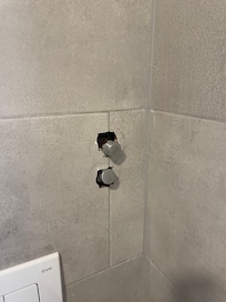 Toilet room tile work. Plumbing valve missing escutcheon plate cover.