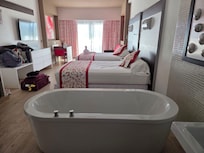 Tub next to bed and behind tub is sink and shower wide open. Shower is frosted but not private