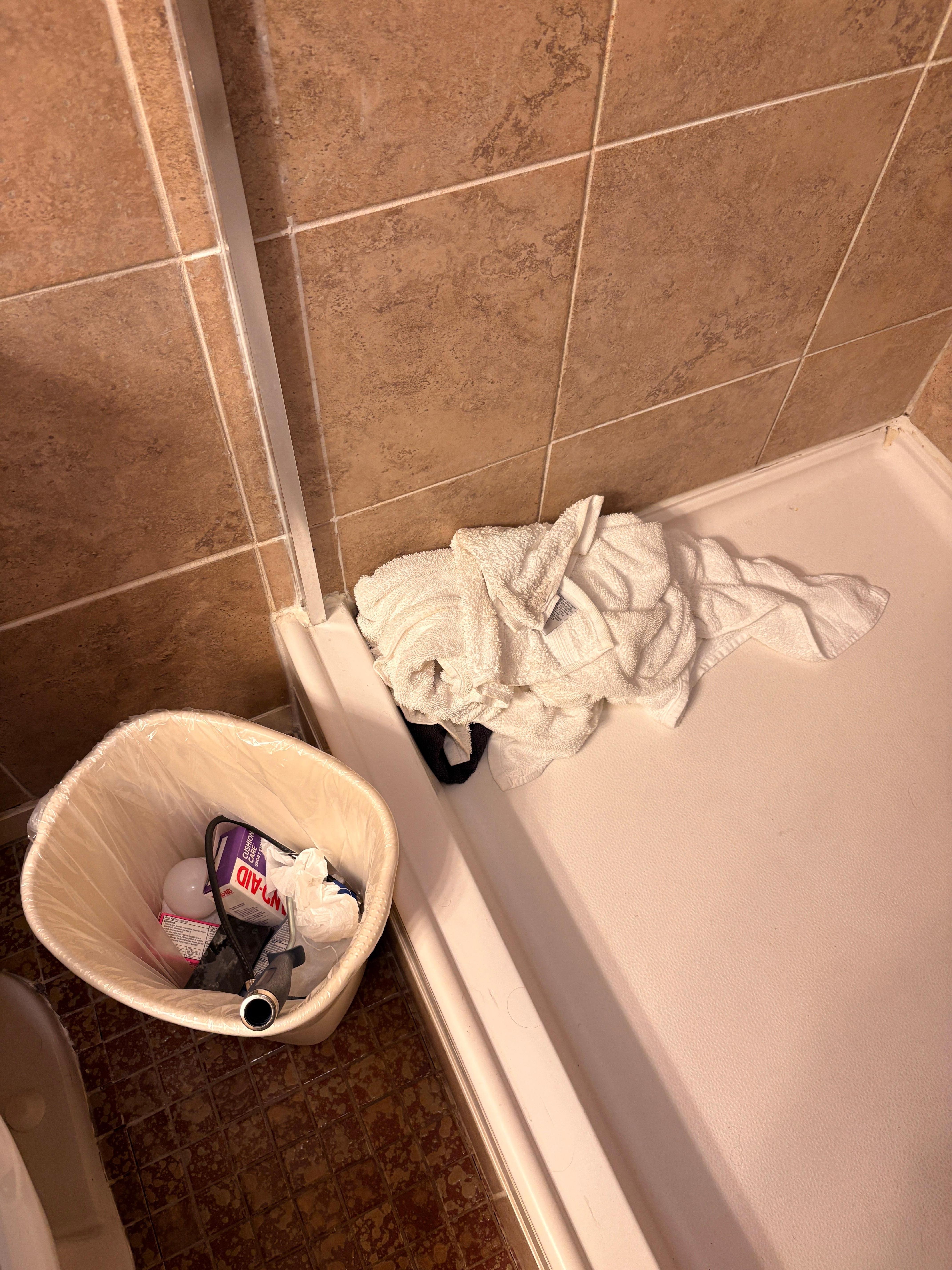 Bathroom full of garbage and wet towels still on shower floor.