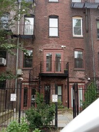 Back of apartment with a small patio and parking spots.