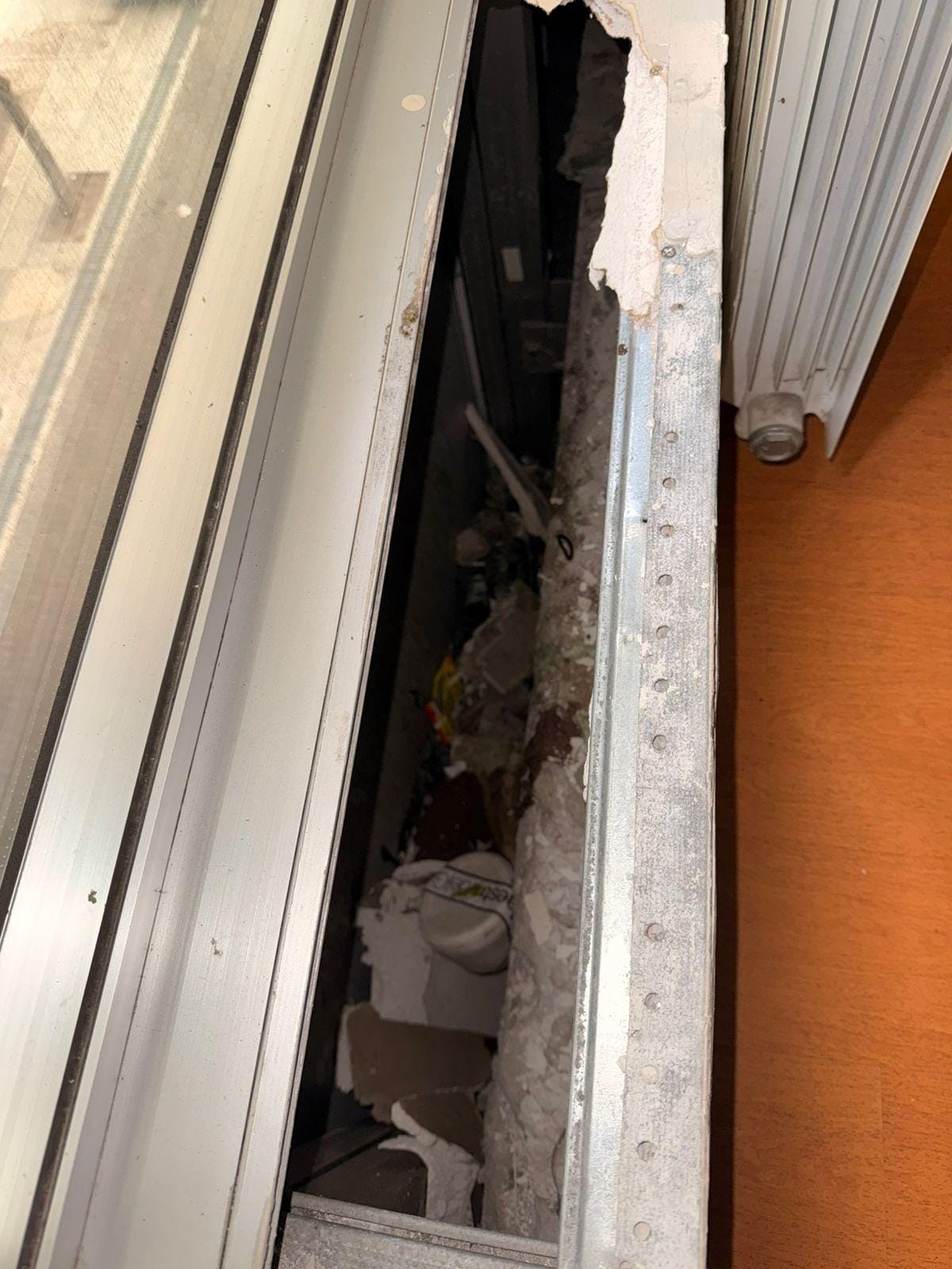 Buraco com entulho e lixo entre a janela e o aquecedor 