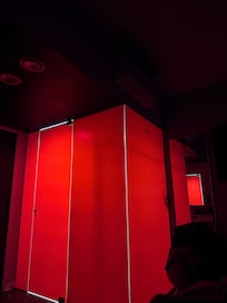 Las paredes del baño son de cristales, tiene pegado un engomado rojo y se ve la sombra de quien esté adentro.