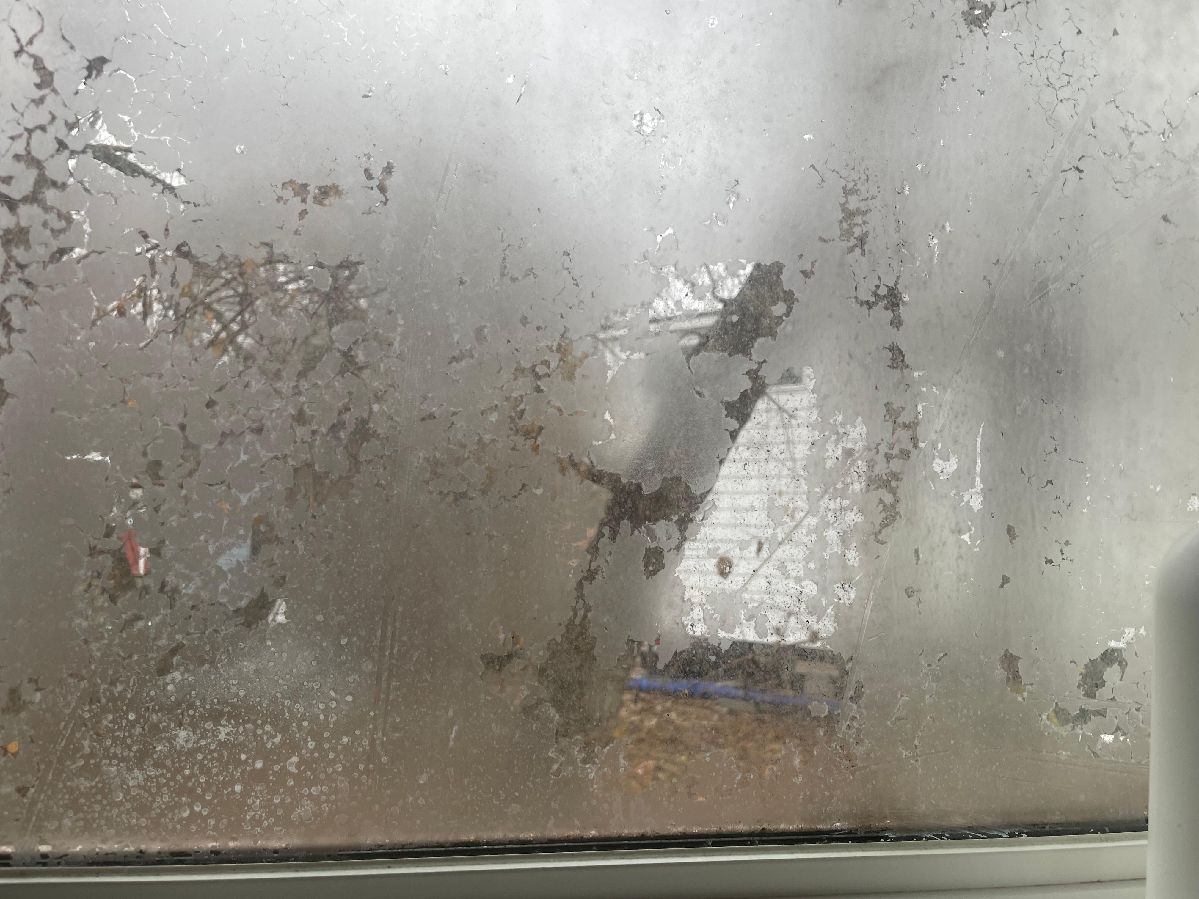 Window in the bathroom with privacy film peeling off. The outside is easily visible.