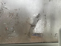 Window in the bathroom with privacy film peeling off. The outside is easily visible.