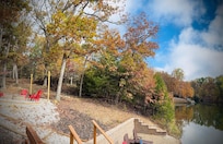 View from lakeside deck showing beach and fire pit with string lights.