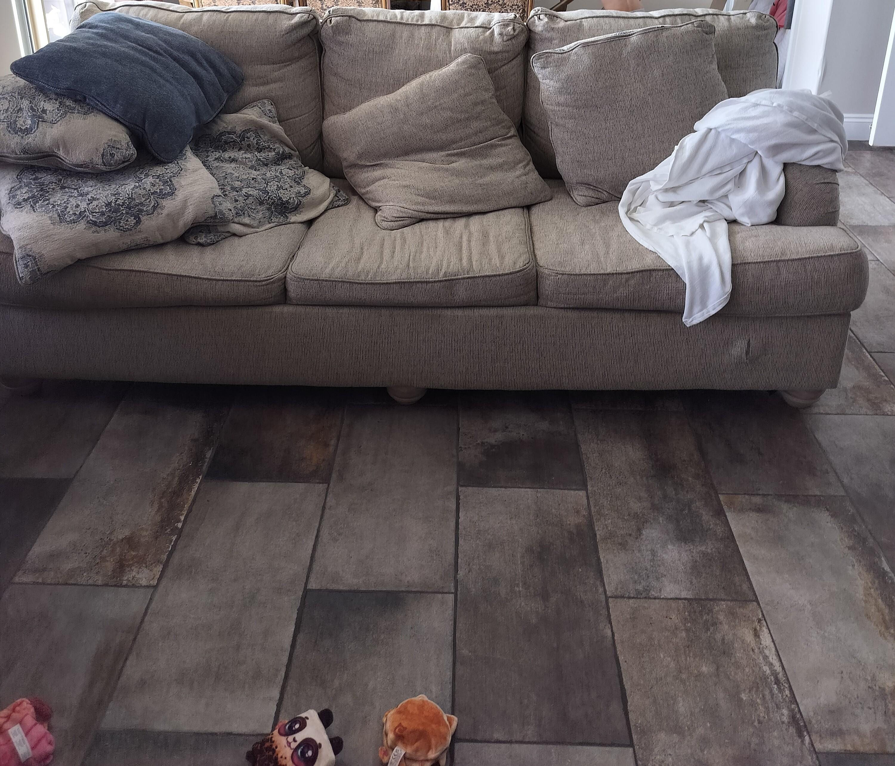 Couch in the living room with rip below the white blanket.