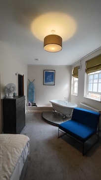 View of the room, including bathtub, iron, ironing board, armchair, drawer