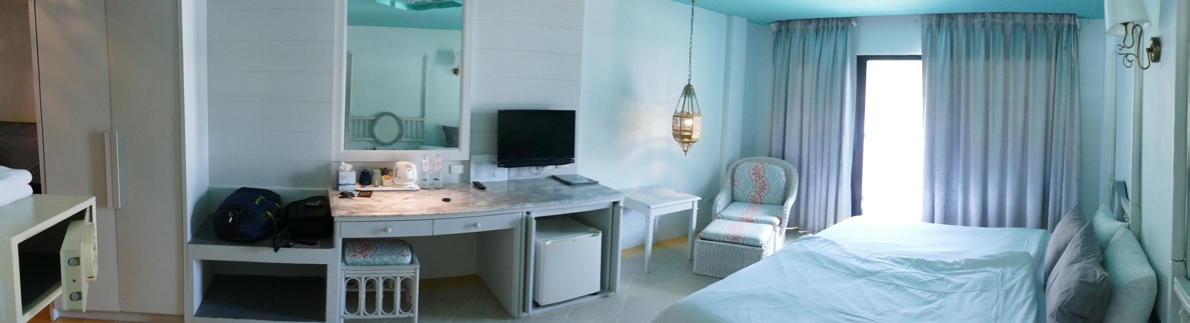 This panorama, from the inside corner by the sink, shows the desk, TV, minibar fridge, and the lounge-chair by the balcony door.