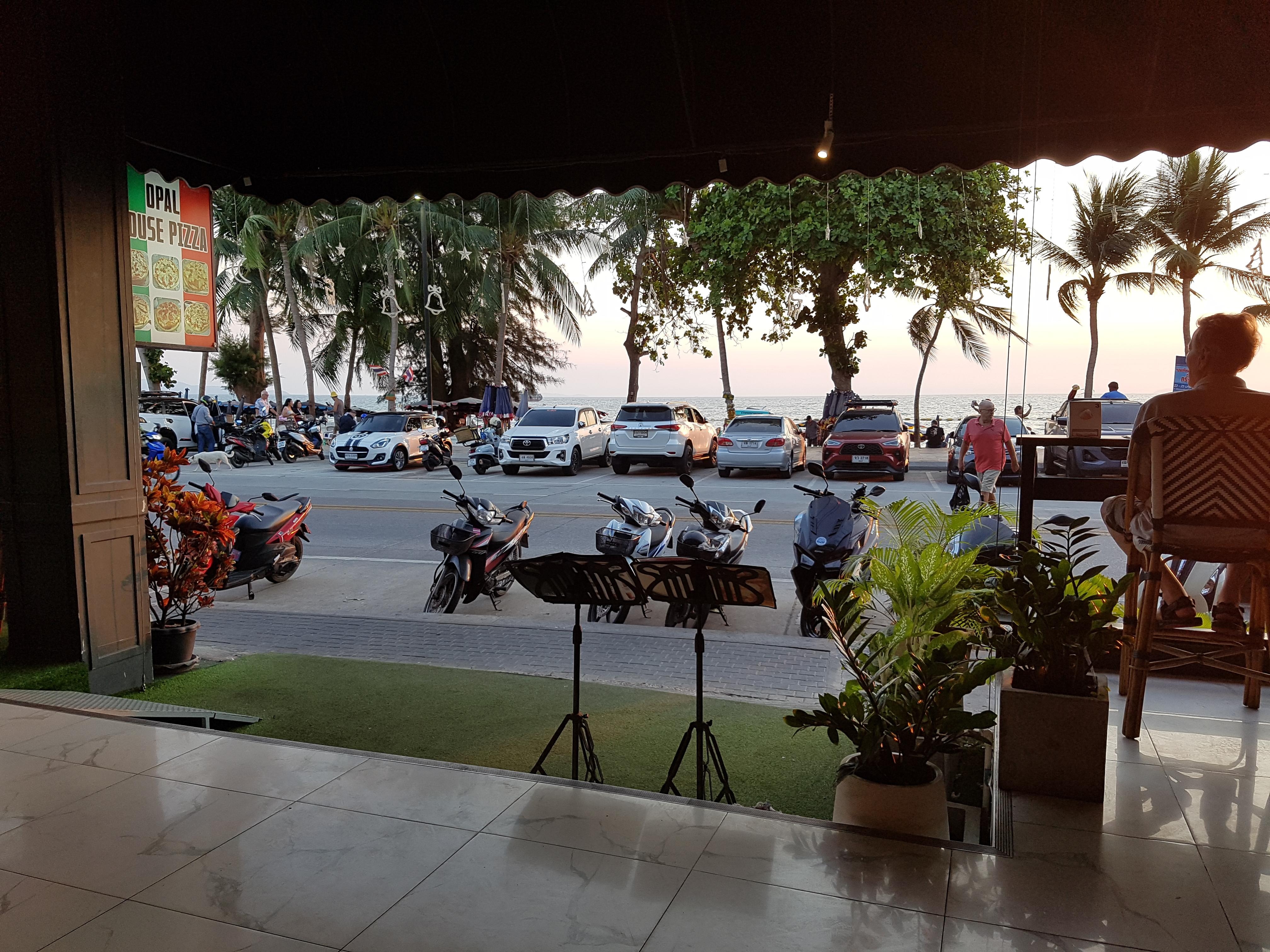 Sitting on high chair at long table looking out to the road and beach as the sun goes down.