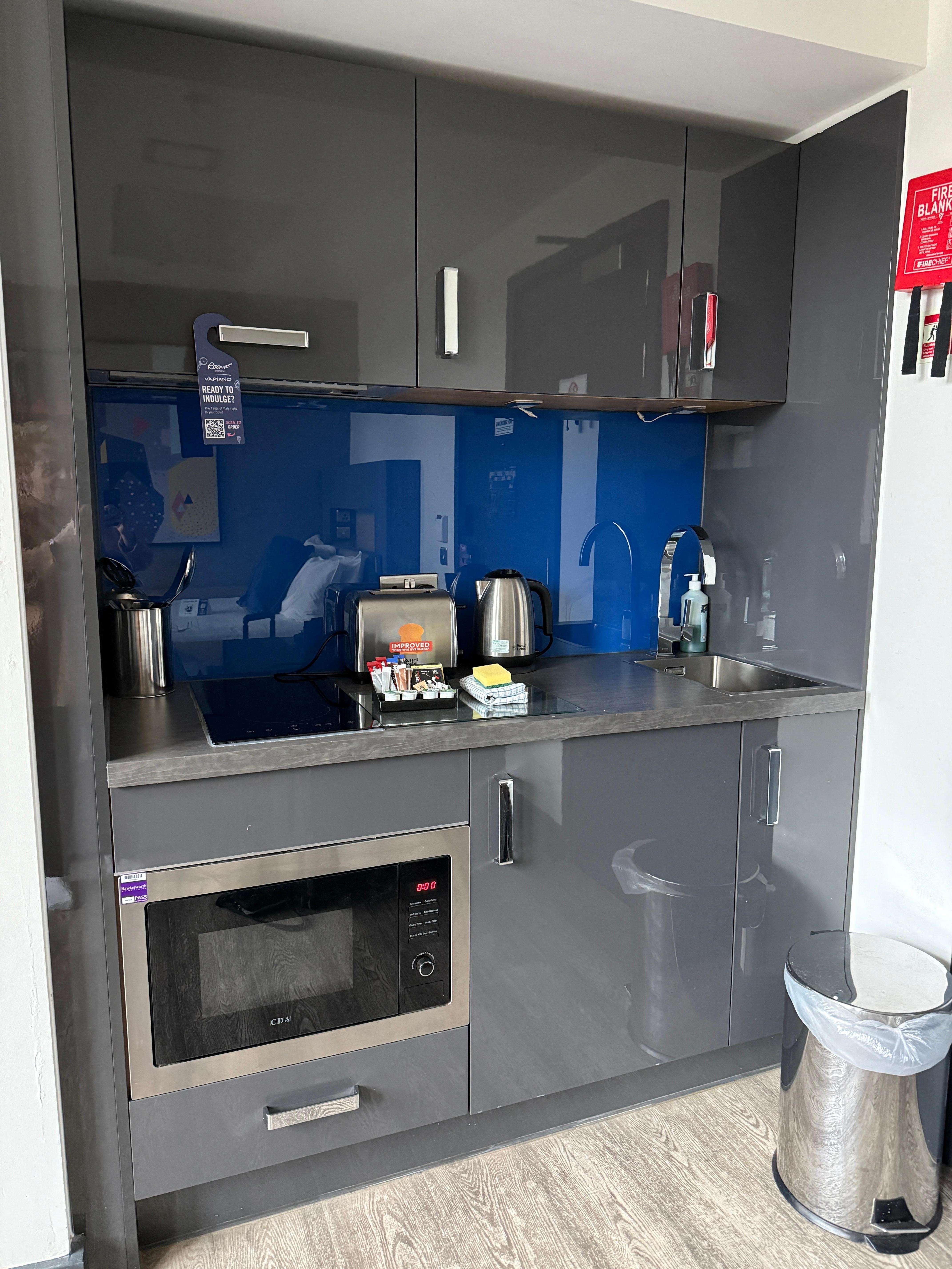 Kitchenette with microwave, fridge, cooktop, oven, kettle, dishes and cutlery.