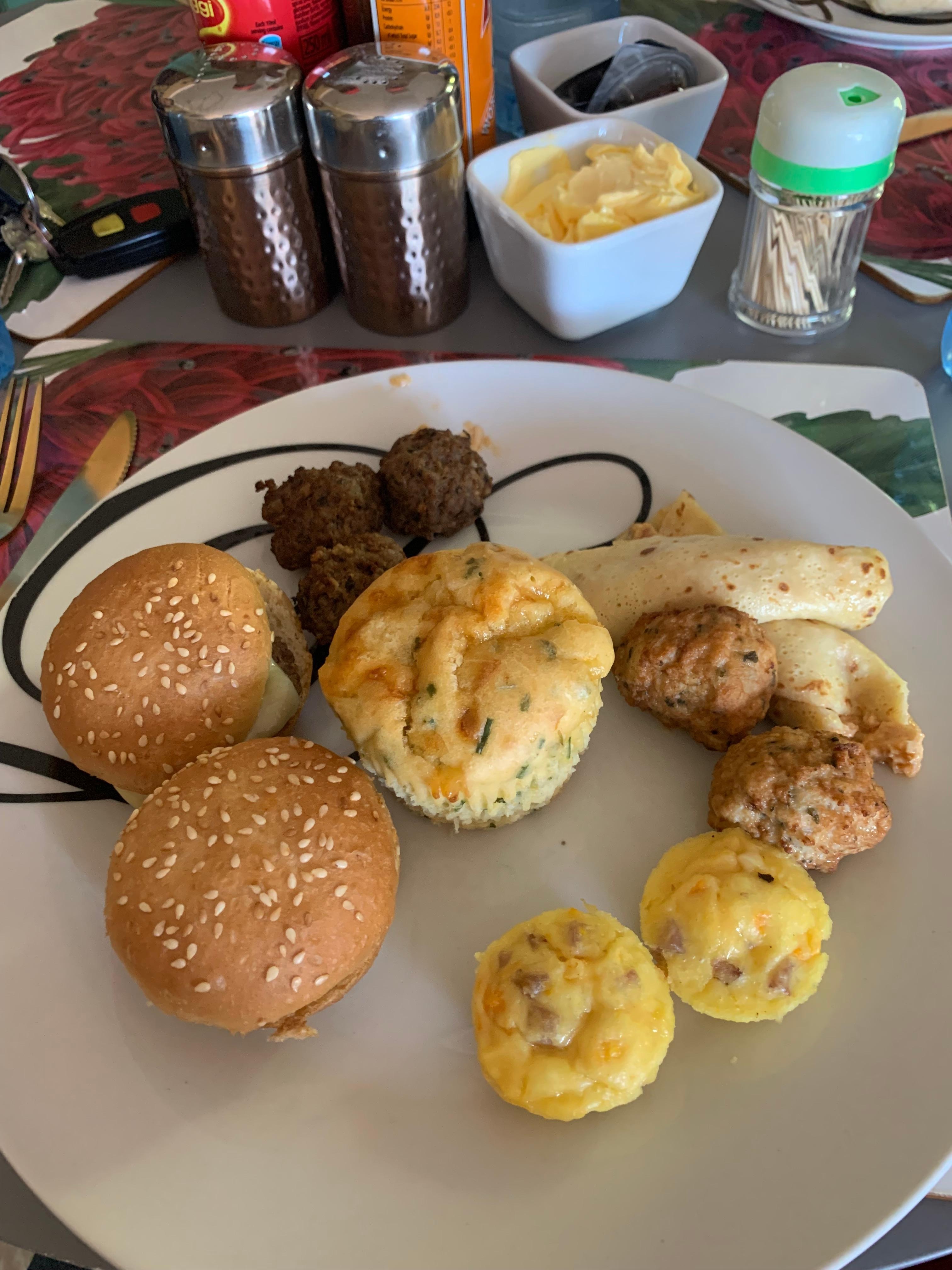 Breakfast consisting of two mini hamburgers, one bacon muffin, 6 meatballs, 3 beef and 3 lam, 2 mini omelets and two pancakes with ragout filling. 