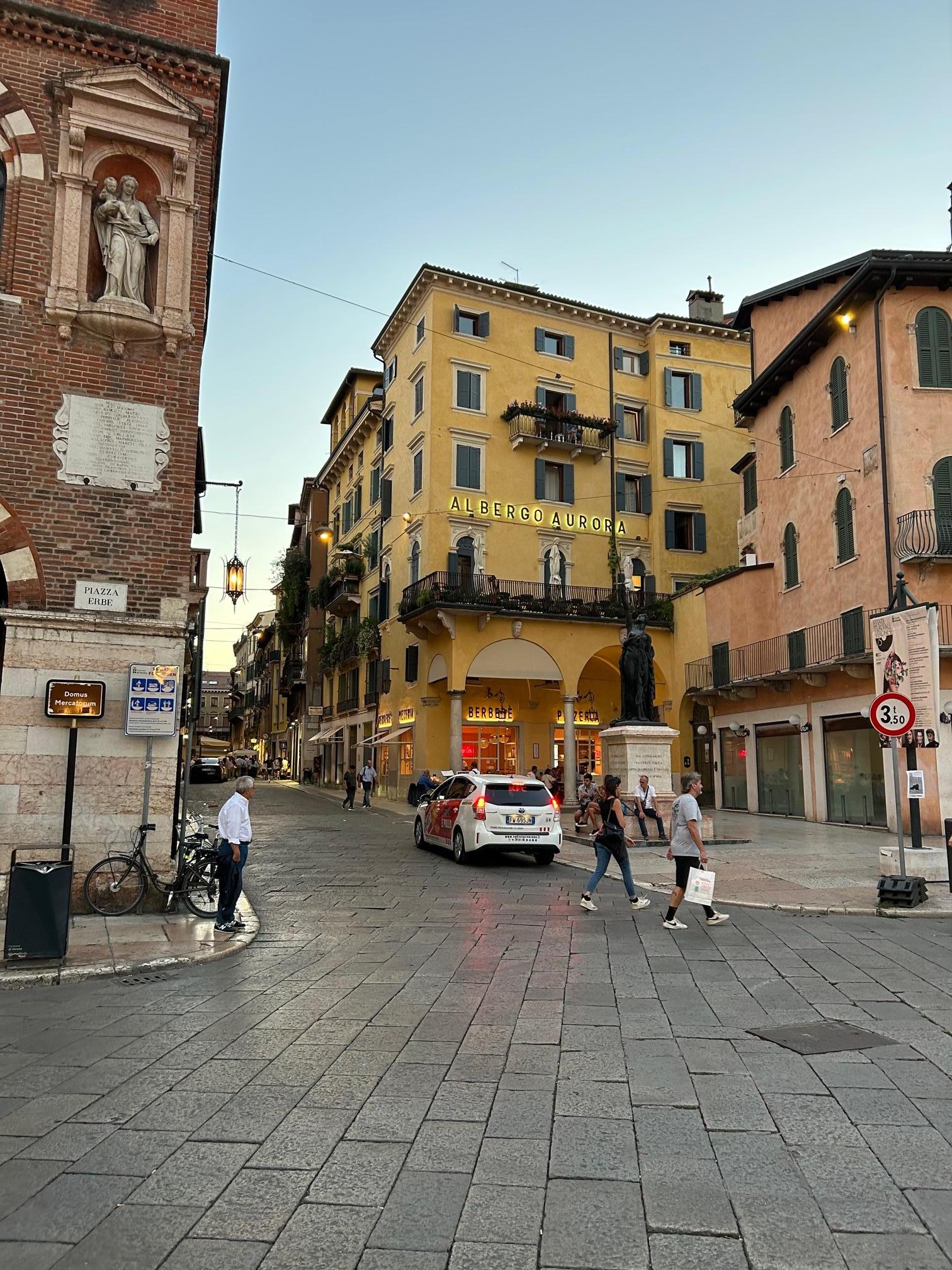 The entrance to the hotel is in the corner of the courtyard next to the pizzeria (behind the statue)