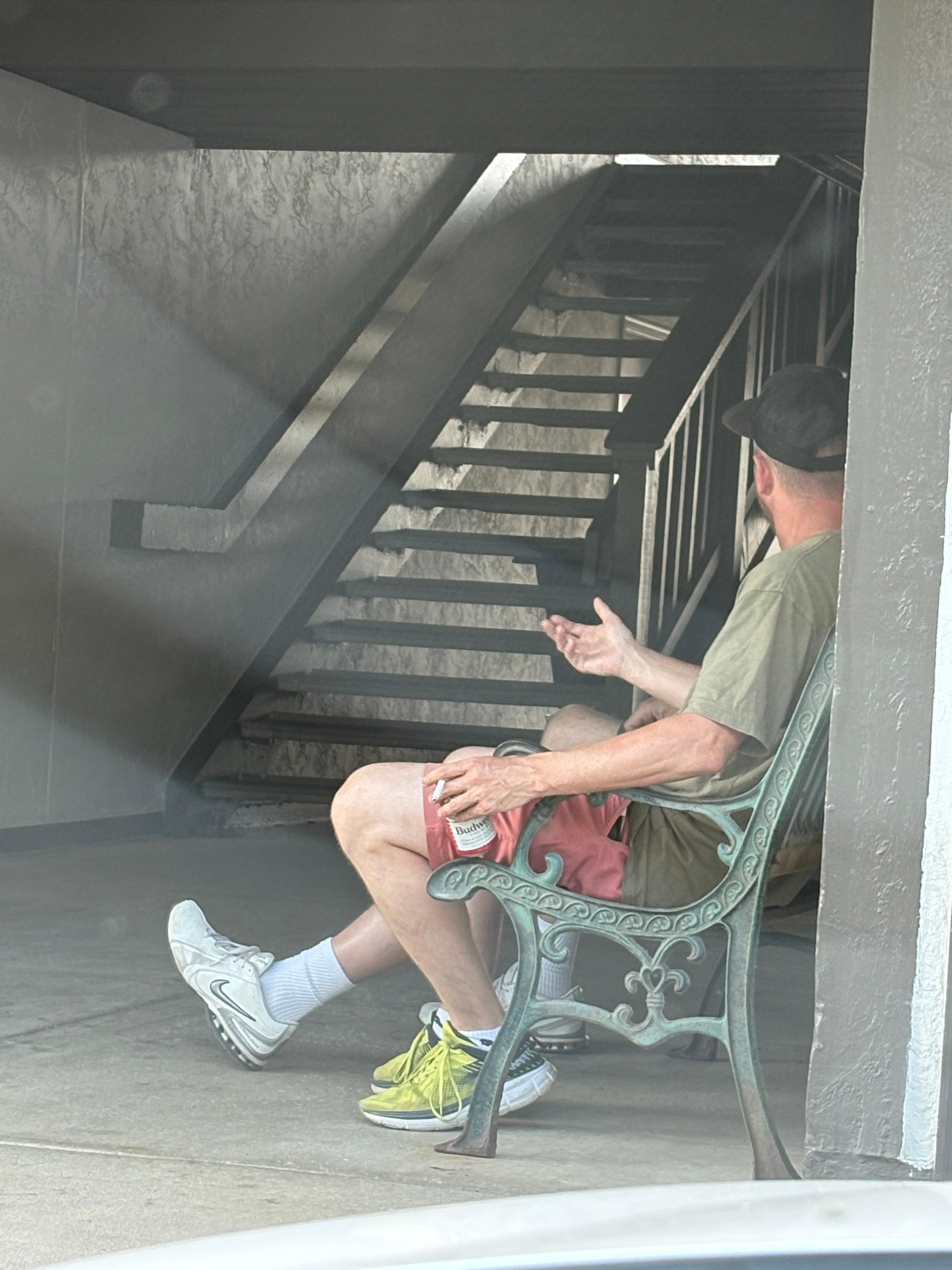 Man drinking beer and smoking a cigarette outside of my room.