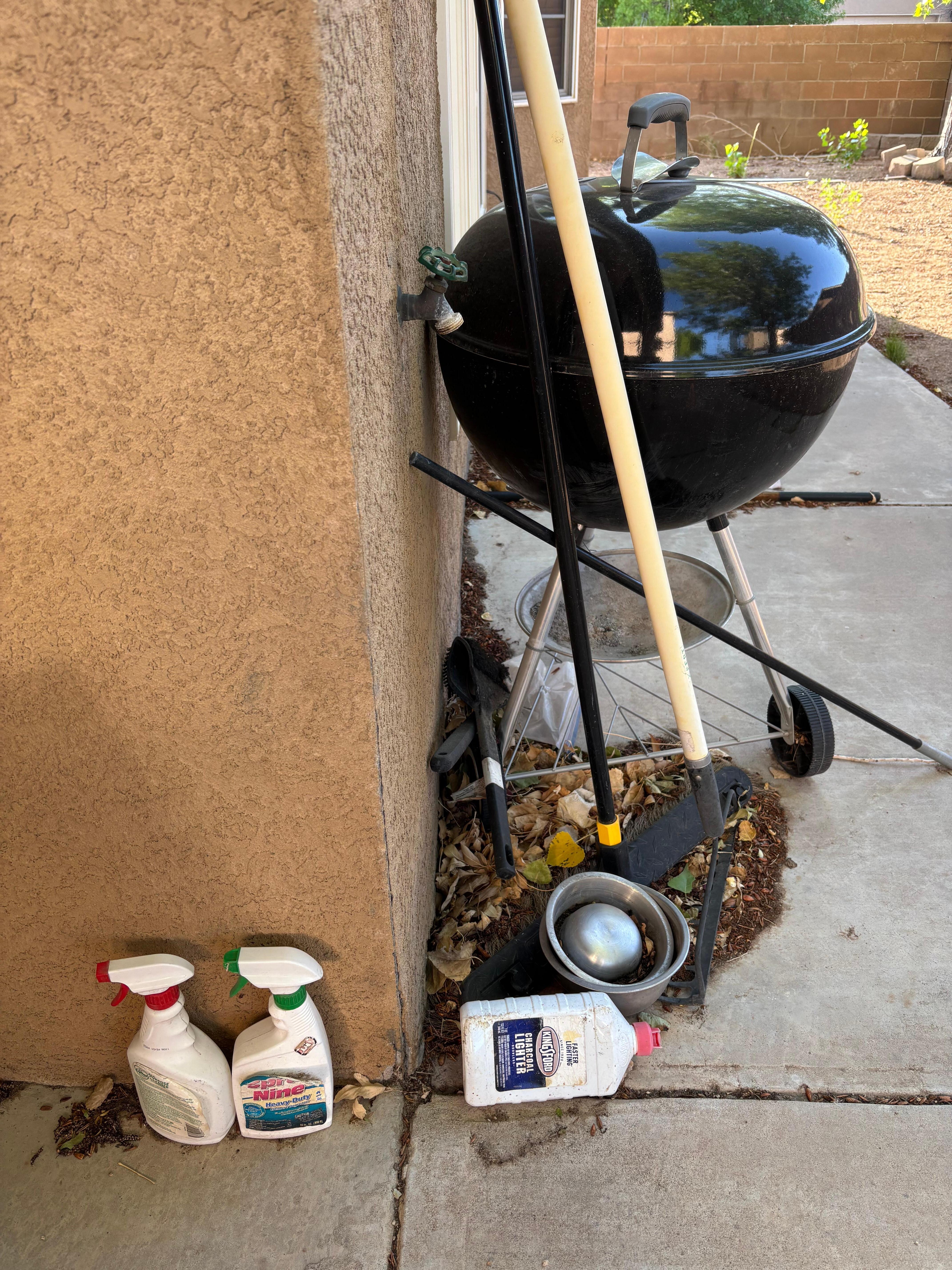 This is the small grill in back yard with spray bottles & charcoal fluid just laying there. 
