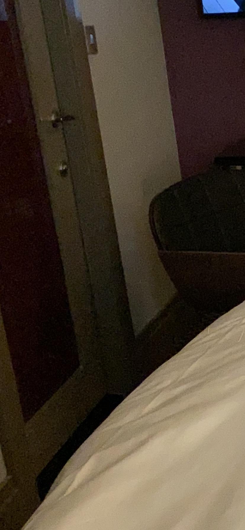 The space between bottom of bed and bathroom door and bed and office type chair.