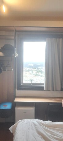 Quarto com janela super segura, a cortina é 100% blackout, ambiente moderno e arrojado, mesa grande com várias lâmpadas, inclusive dos lados da cama e coitada para mesa, cabides, várias prateleiras mesinha de cabeceira, cadeira para sentar e coberta.