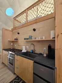 Kitchenette inside Dome 1 with loft bed above and bathroom beneath
