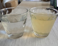 Glass on the right has yellow water from bathroom sinks. water on right is from water bottle