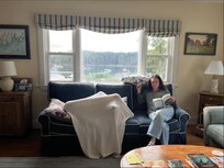 J reading on sofa near picture window; a child Z is playing with a blanket.
In livingroom.