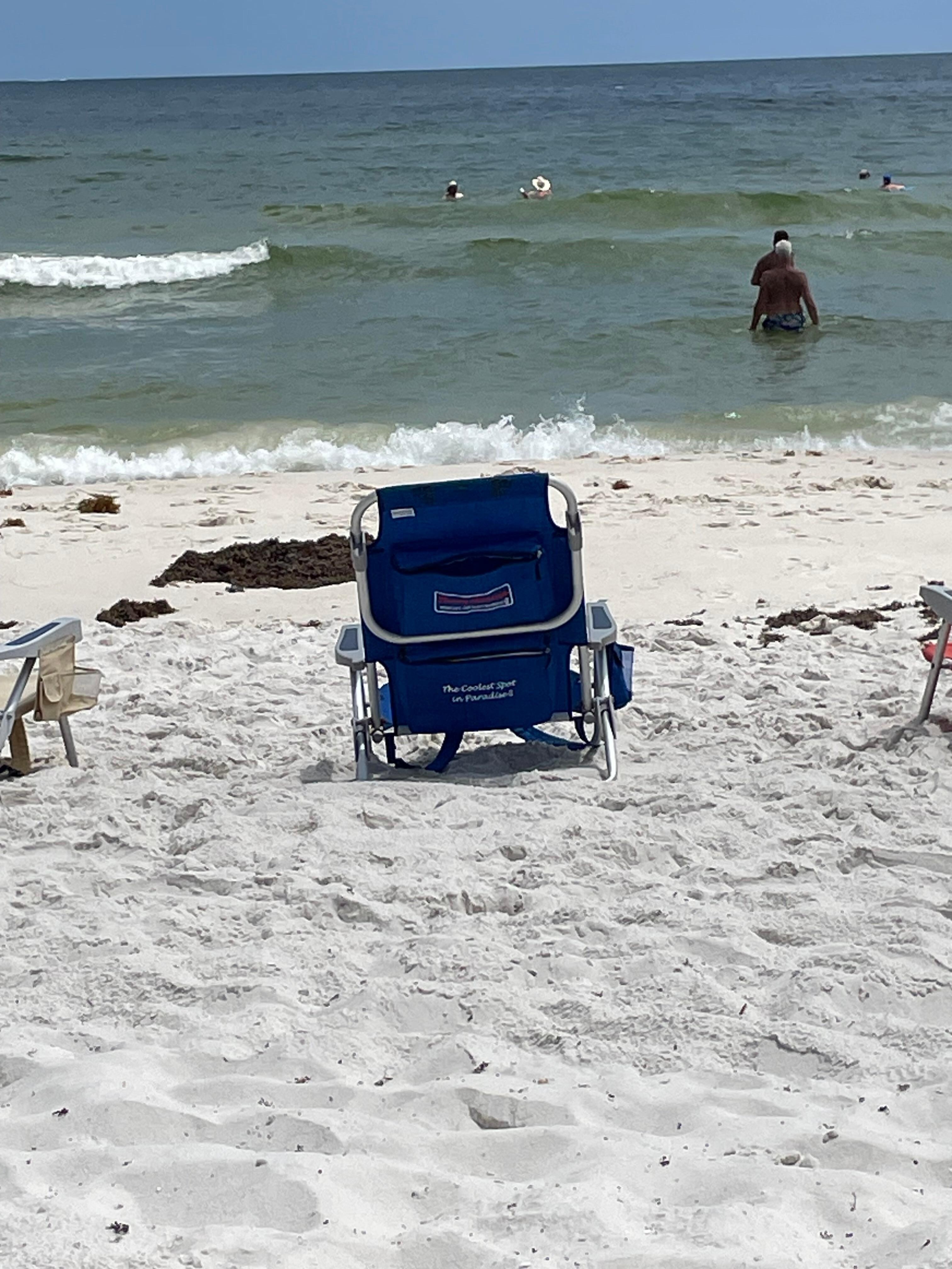 Empty beach chair and people in the water 