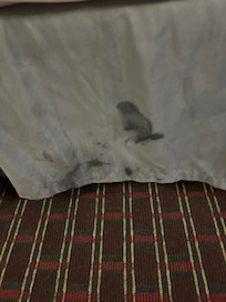Stain on bed skirt below stain on sheets.