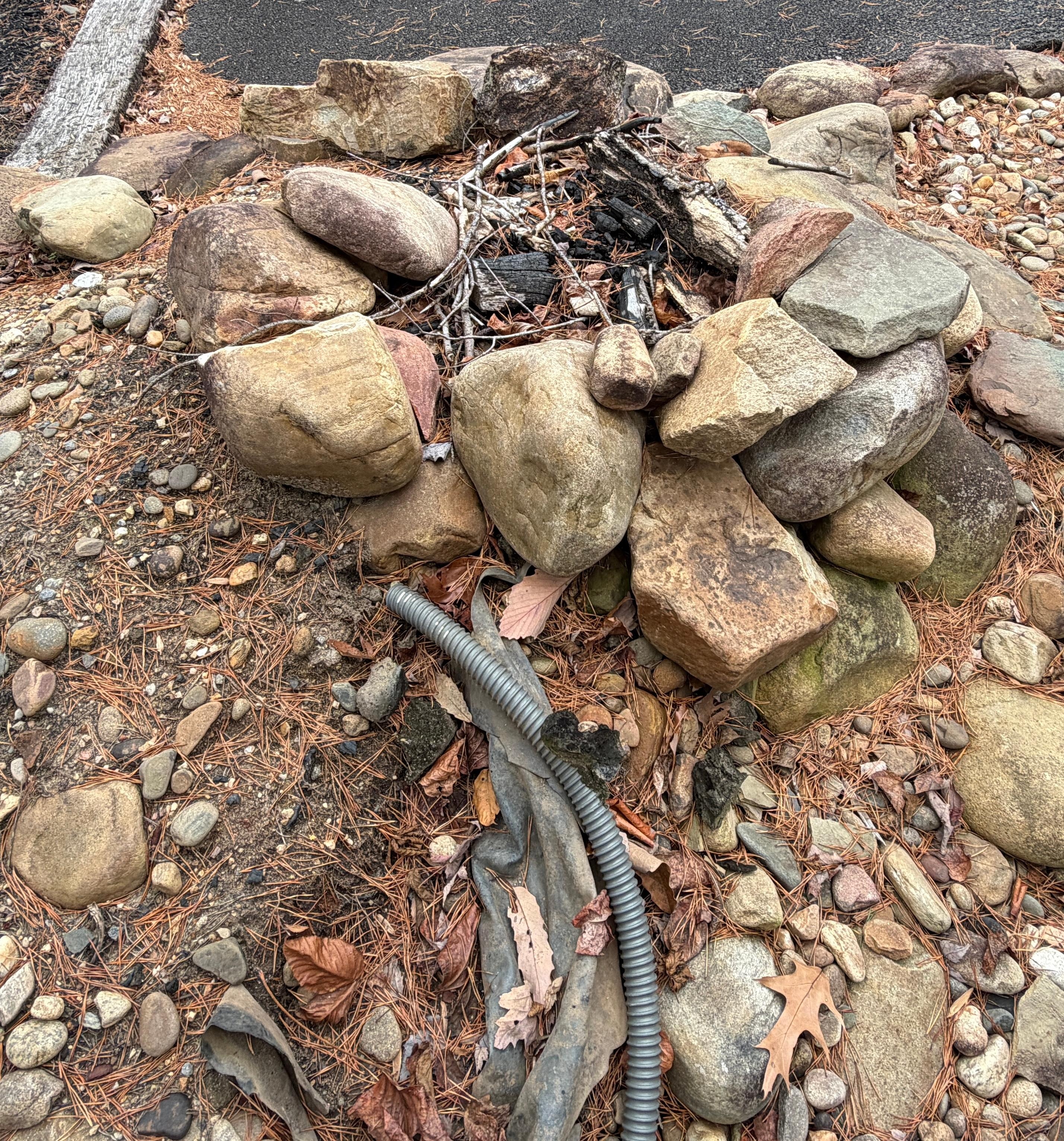 Outdoor fire pit made of loose rocks with exposed plastic tubing. 