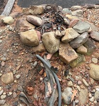 Outdoor fire pit made of loose rocks with exposed plastic tubing.