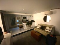 Couch/living room area at entry door w/ kitchen in background, and laundry & bathroom beyond that.