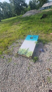 Corn hole warped with weeds growing out.