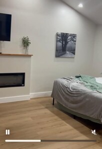 Bed open to living room (electric fireplace) and kitchen to the left.