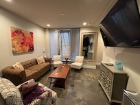 View of living room from kitchen. Full kitchen has sink, oven, microwave & Fridge. There’s a giant TV on the wall.