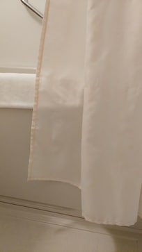 Formerly white bathroom curtain, now pink with mold, in contrast with the shower mat towel