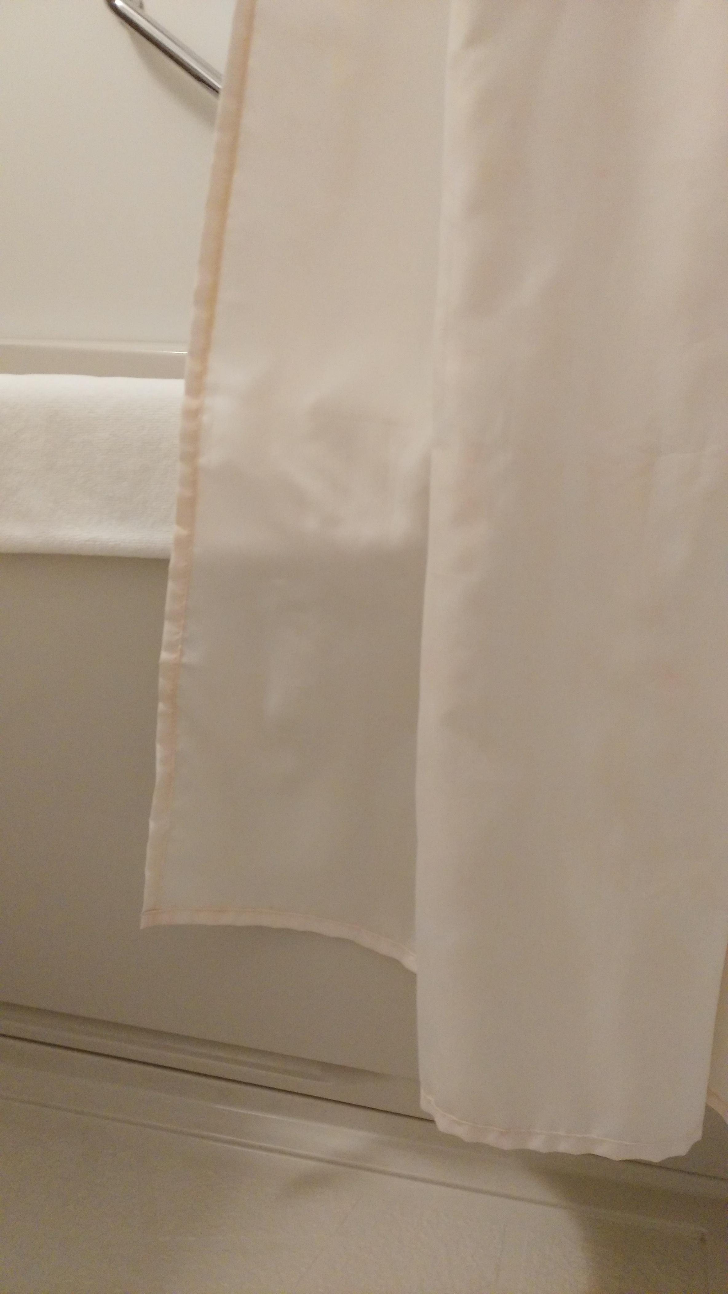 Formerly white bathroom curtain, now pink with mold, in contrast with the shower mat towel