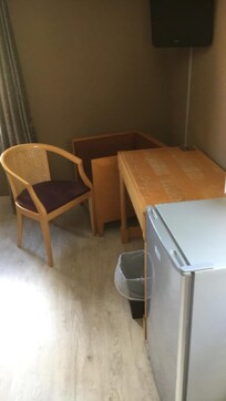 Mobilier de chambre vieillot avec trace devant rond de verre et frigo vide bruyant