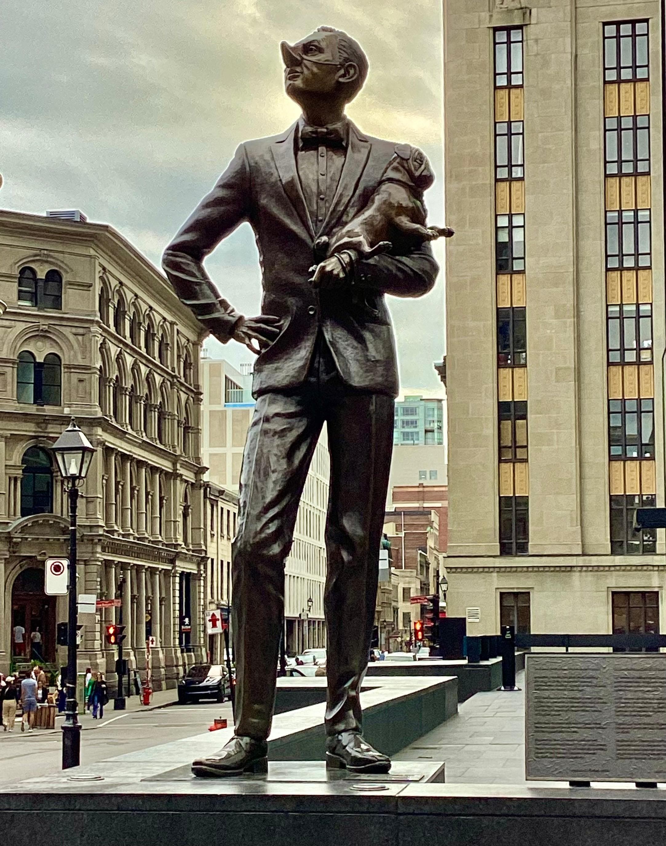 Satirical statue of a snooty man holding his pug, the man having a long haughty nose turned up in disapproval of nearby Notre Dame  Basilica, in the park near the apt.