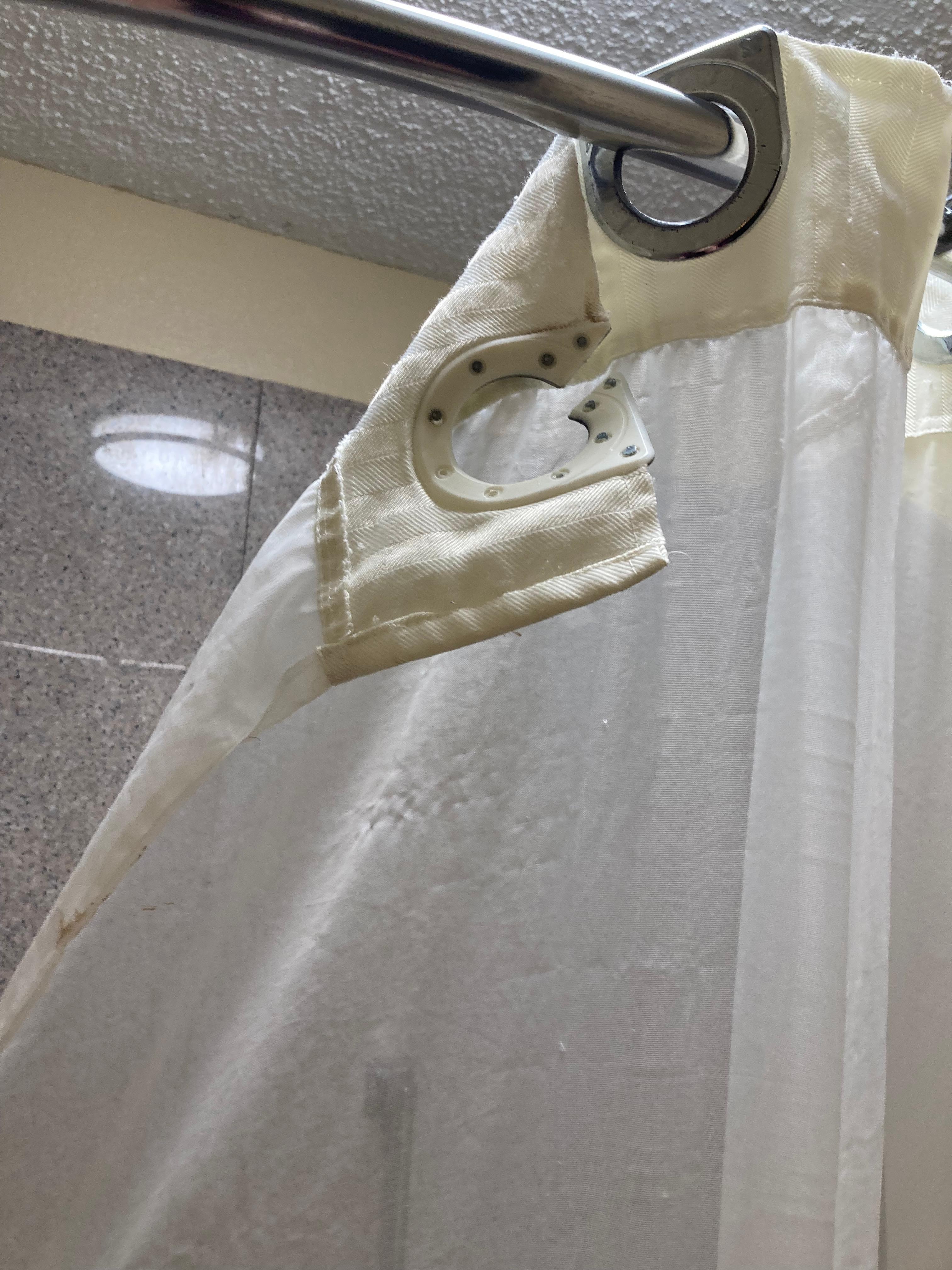Shower curtain broken and stained with mildew and other unidentifiable stains.
