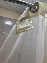 Shower curtain broken and stained with mildew and other unidentifiable stains.