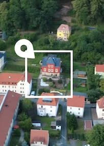 Ein aktuelles Luftbild (Distanzaufnahme mit Drohne) des Gebäudes. Die Farbe des Gebäudes hat sich von gelb zu rot geändert. Die FeWo befindet sich im mittleren Geschoss (4 Fenster zur Straße)