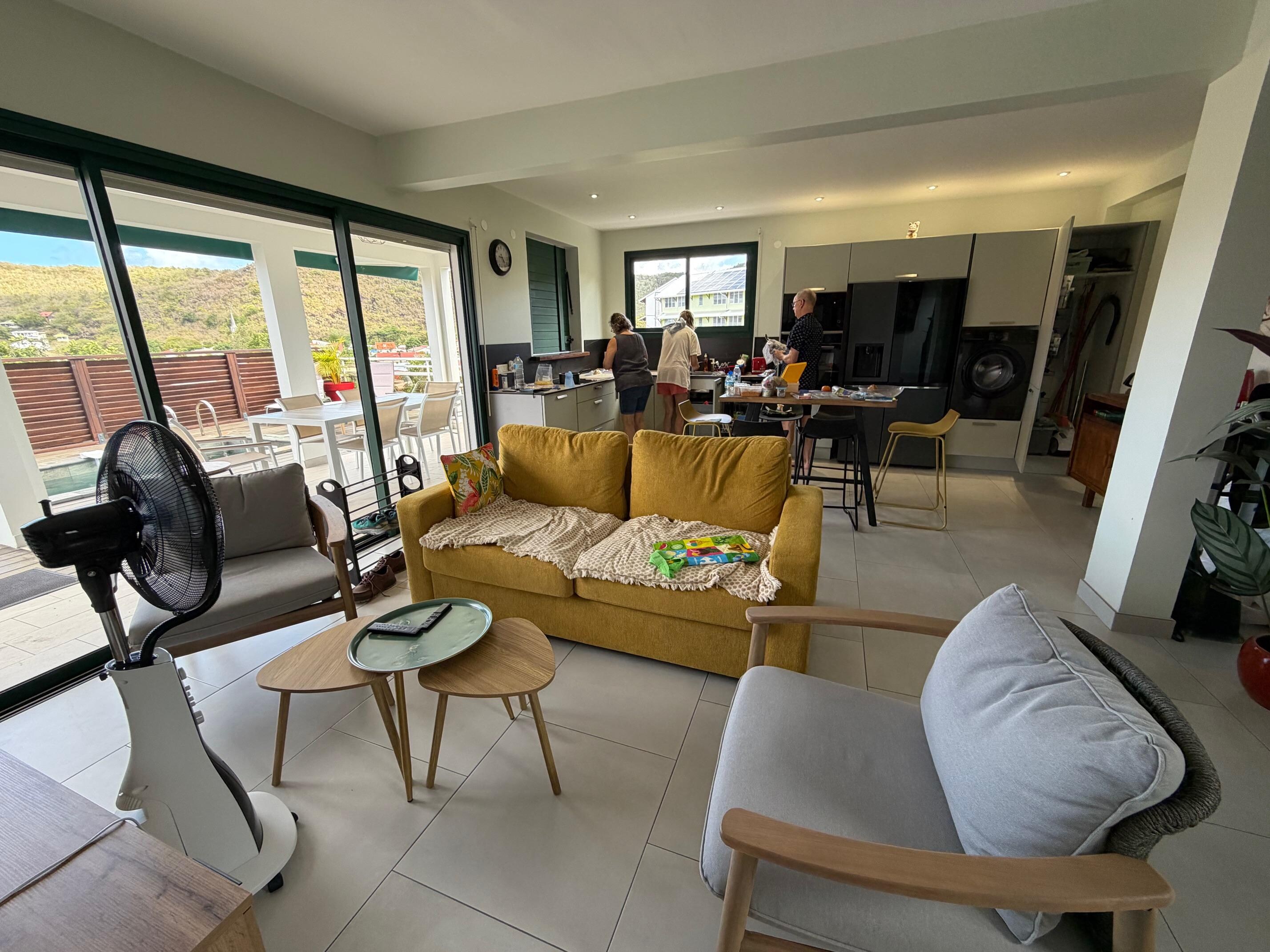 This view shows the modern, well-equiped kitchen at the back, and the dining room table and pool outside the sliding door.