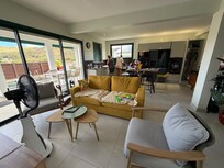 This view shows the modern, well-equiped kitchen at the back, and the dining room table and pool outside the sliding door.