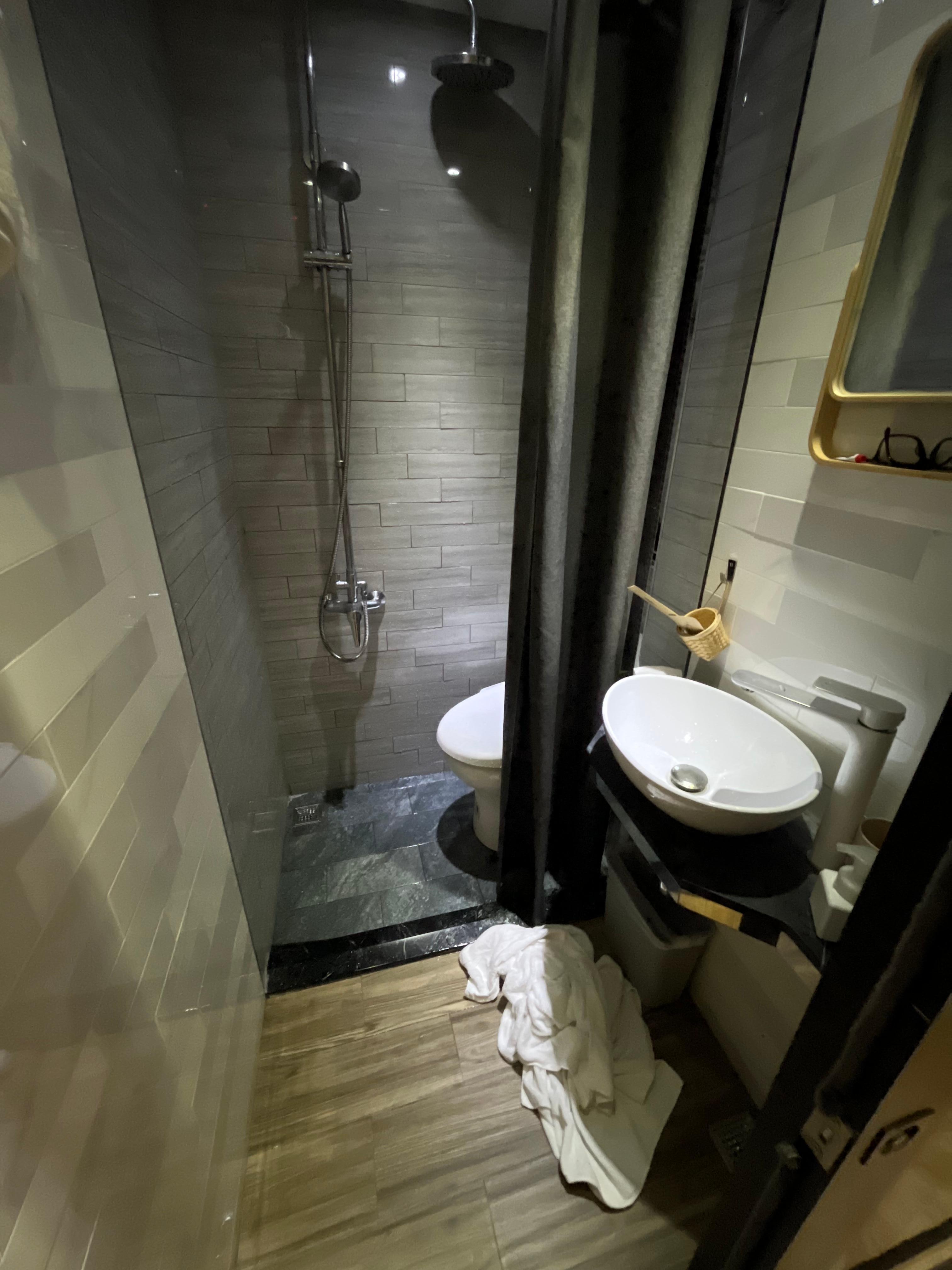 Tiny bathroom with shower over the toilet. Towels on the ground to soak up all the water that sprayed past the shower curtain. 