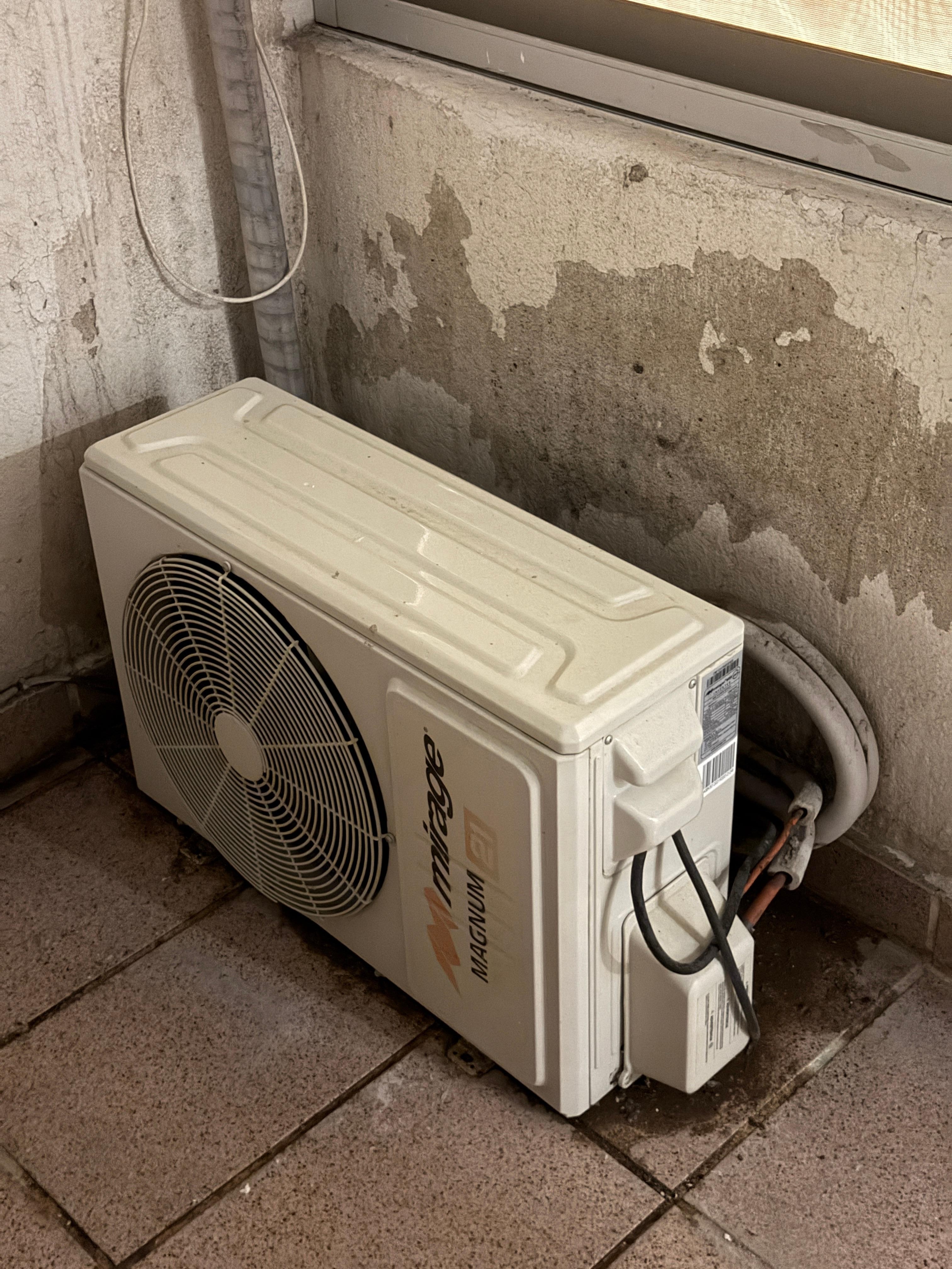 One of numerous air conditioner compressors attached to the wall in light well, right next to sleeping area.