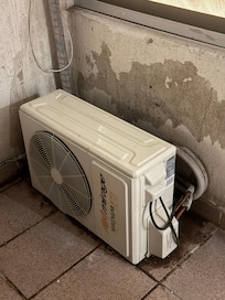 One of numerous air conditioner compressors attached to the wall in light well, right next to sleeping area.