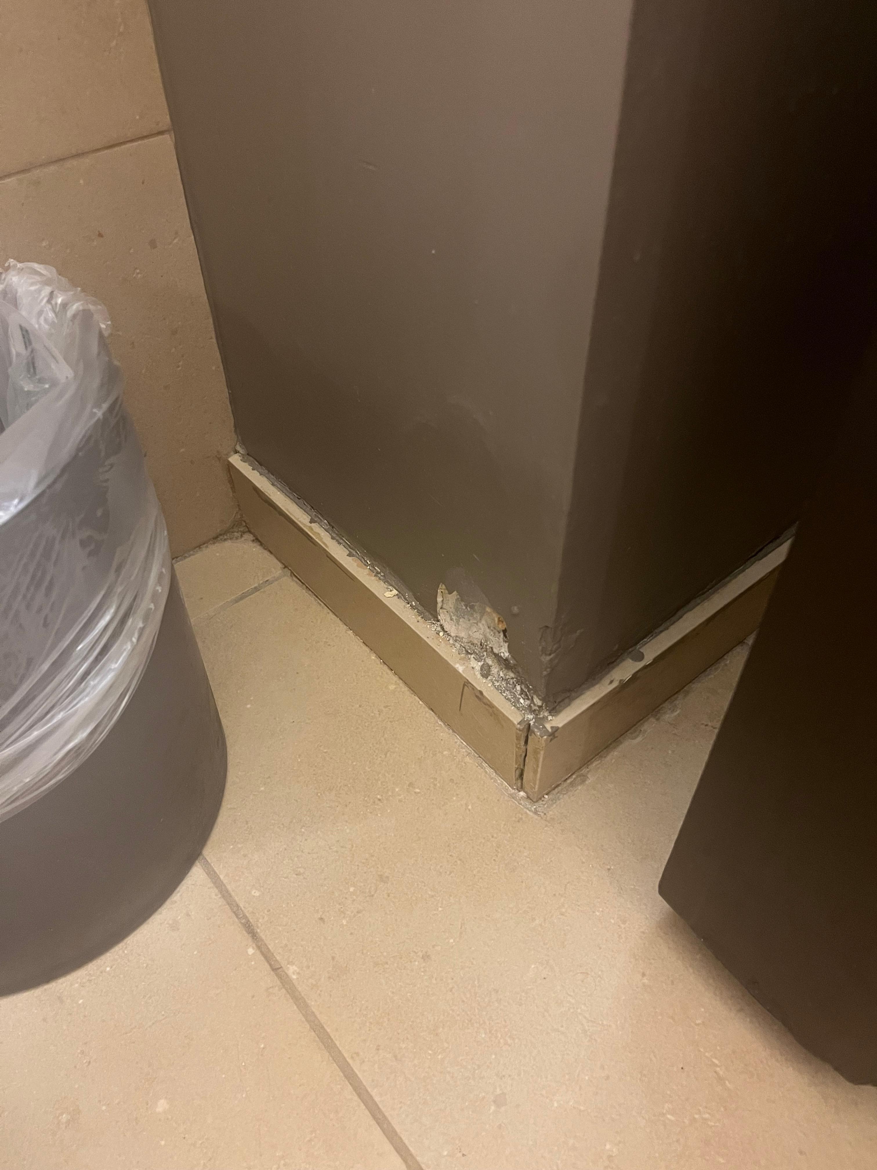 In bathroom next to toilet, massive dent in drywall. The trim along the bottom of the wall was poorly secured.