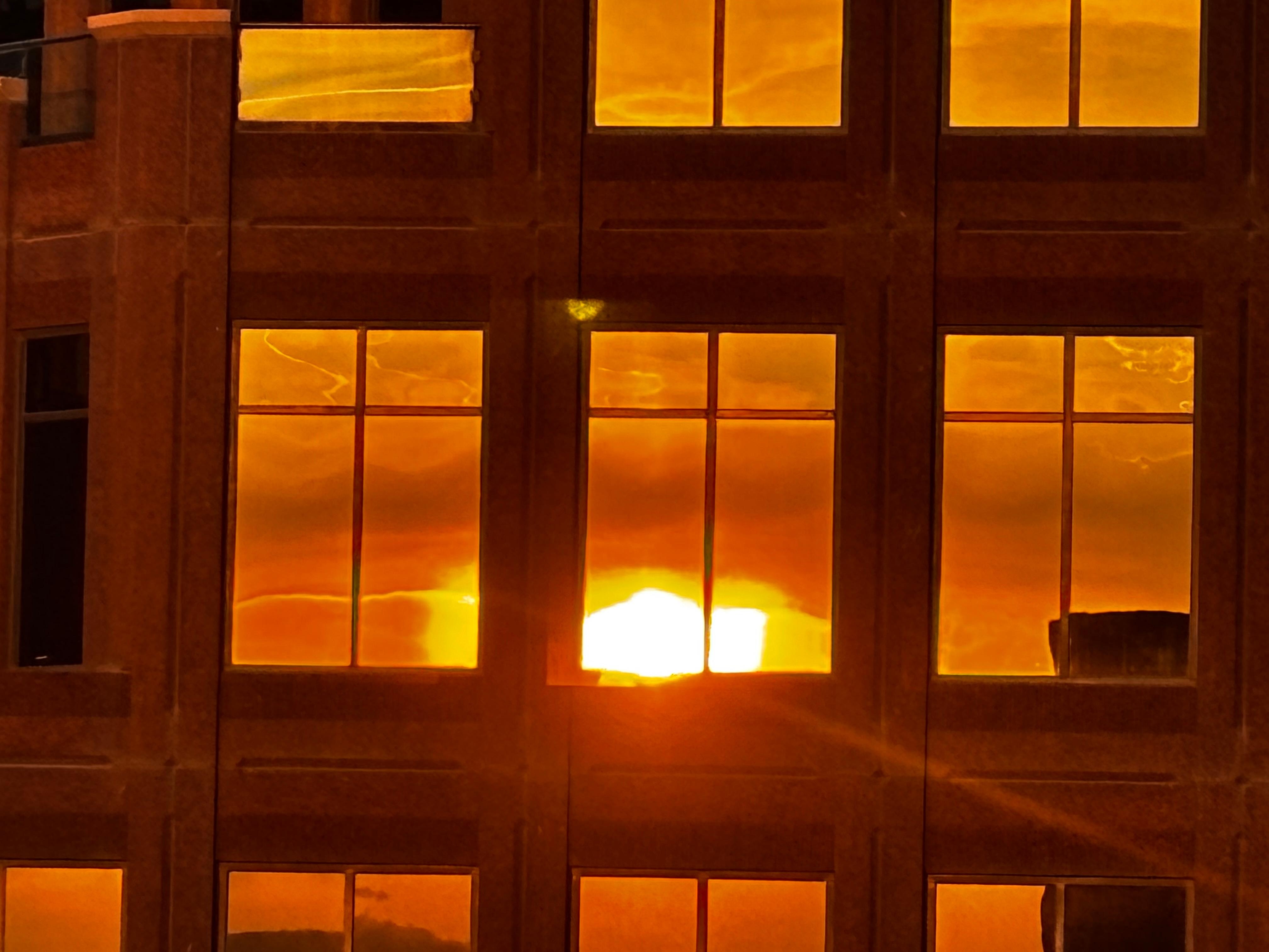 Looking west from my hotel window, the sunrise reflected in the building across the street .