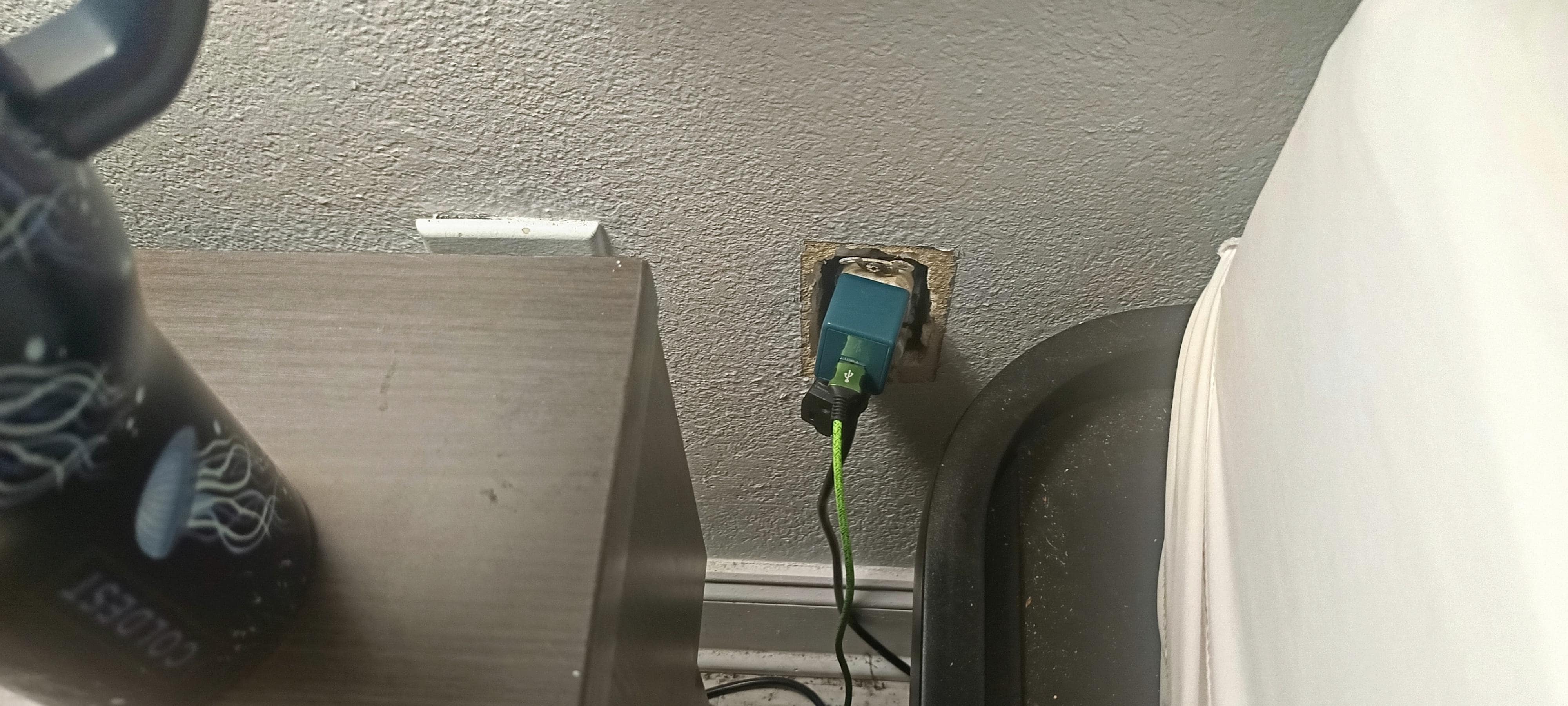 Uncovered outlet vicariously positioned next to bed.