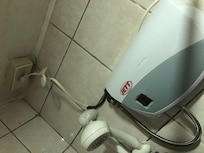 Hot water heater in the shower with ungrounded plug above. Note: the wire coming out of the heater is wrapped with electrical tape. UNSAFE
