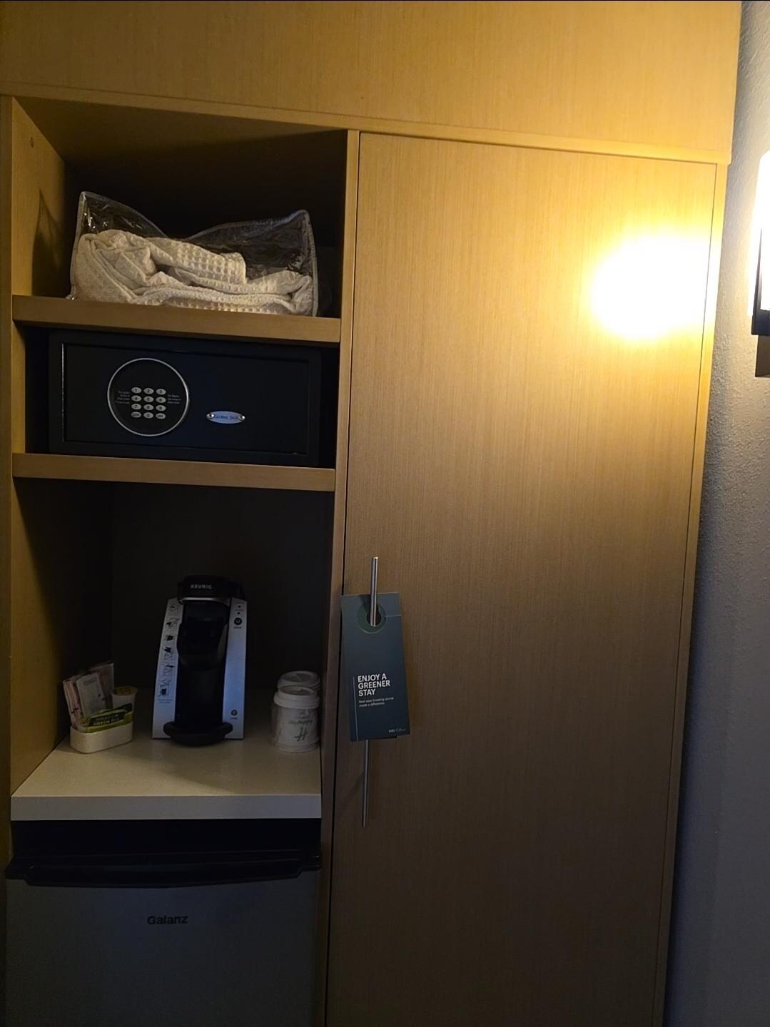 Safe, fridge, keurig and behind the door is iron, board and closet.