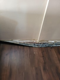 The baseboards falling away from the walls in the room.