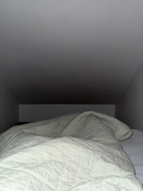 Small slanted closet with bed that provides less than a foot a walking space against the wall.